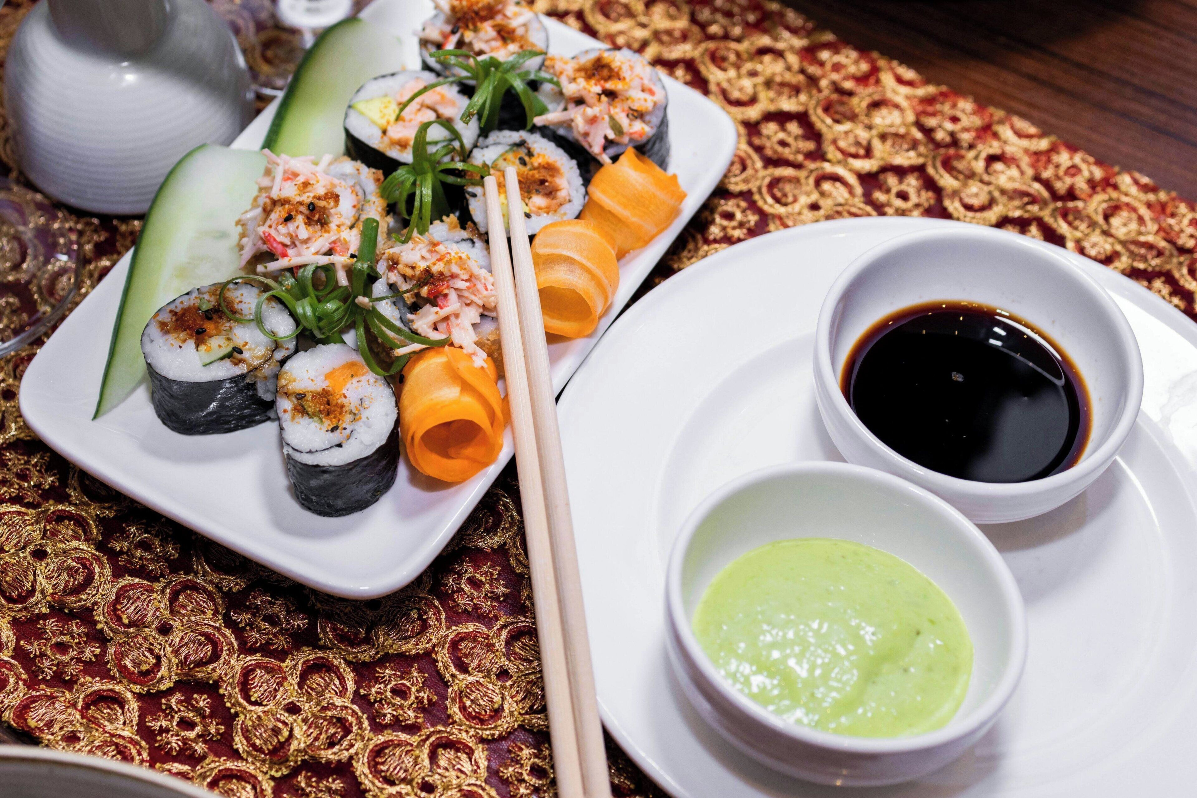 A plate of sushi with two dipping sauces and a decorative tablecloth.
