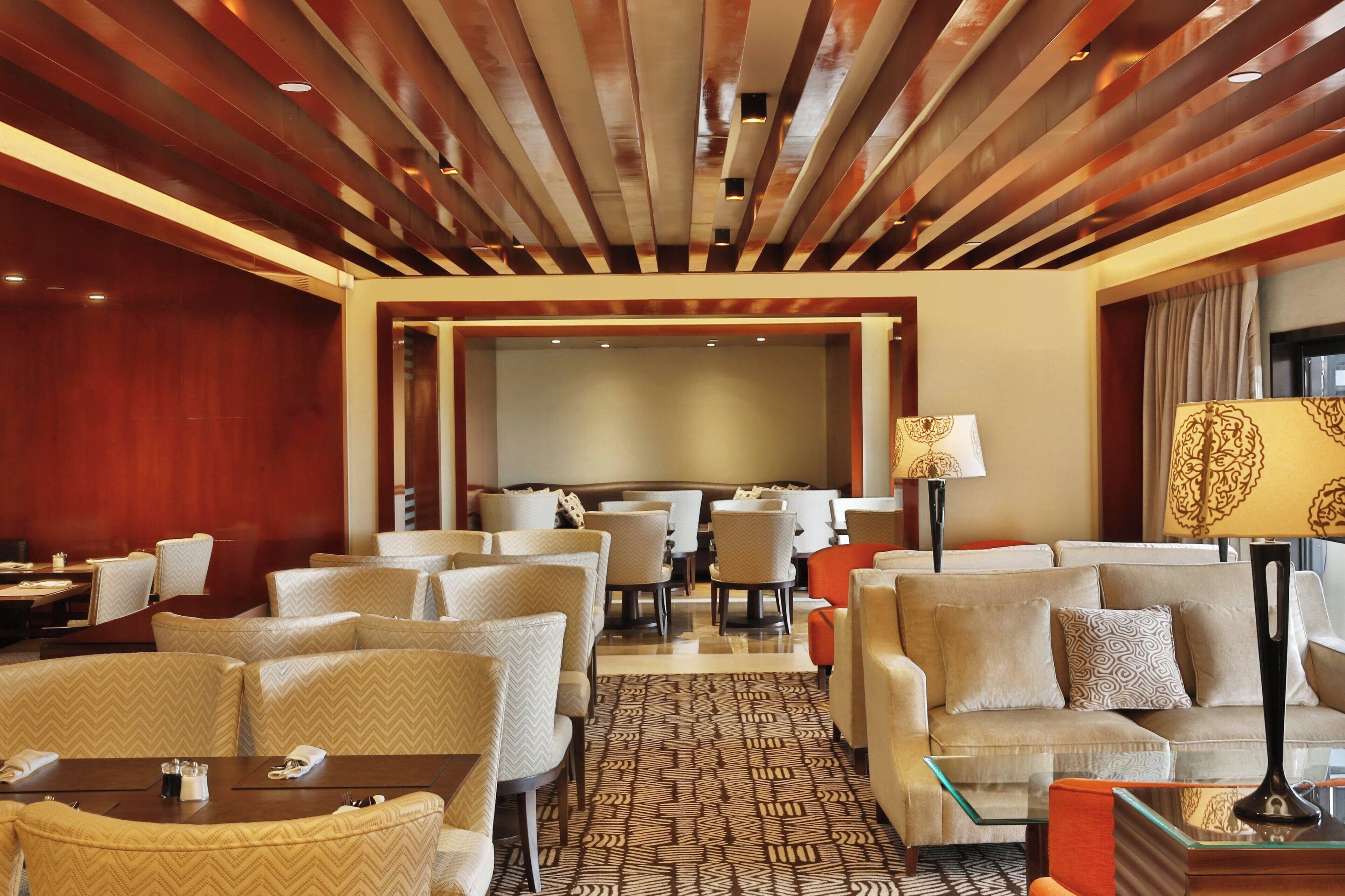 Un vestíbulo de hotel con diseño moderno, que presenta una combinación de zonas de estar, un espacio central para comer y una pantalla grande para presentaciones.