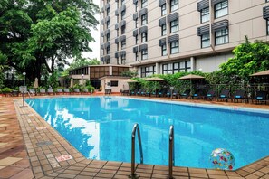 Una piscina con solárium azulejado, sillas de descanso y sombrillas.