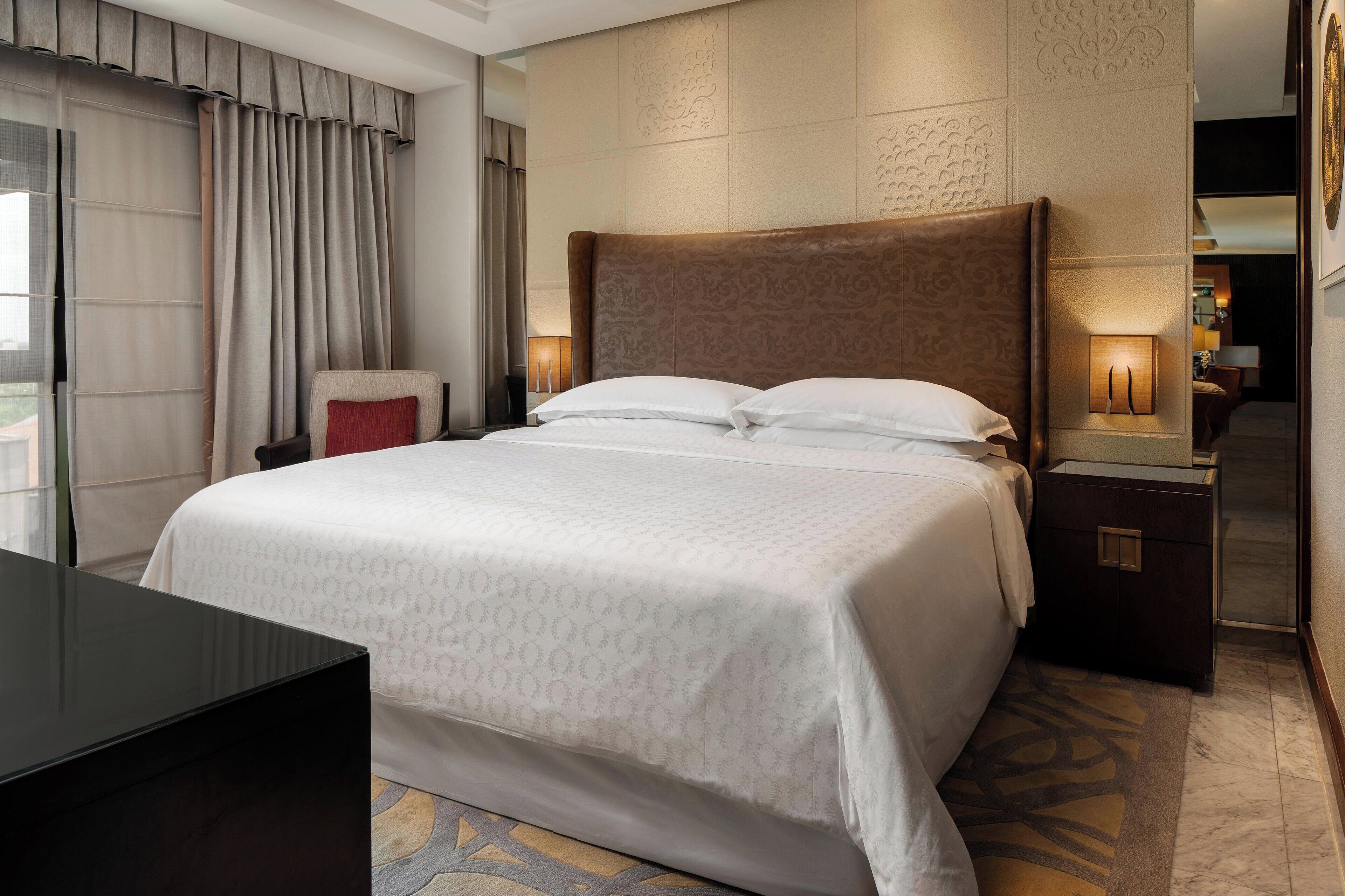 A hotel room with a large bed, a nightstand, a desk, and a window with curtains.