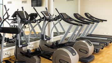 Una fila de cintas de correr y elípticas en un gimnasio con piso de madera y paredes blancas.