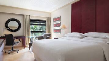 Habitación de hotel con una cama grande, un escritorio con silla, un espejo redondo y una ventana con cortinas.