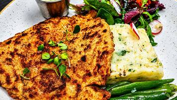 Une assiette composée de viande grillée, de purée de pommes de terre, de haricots verts et d’une salade de radis.