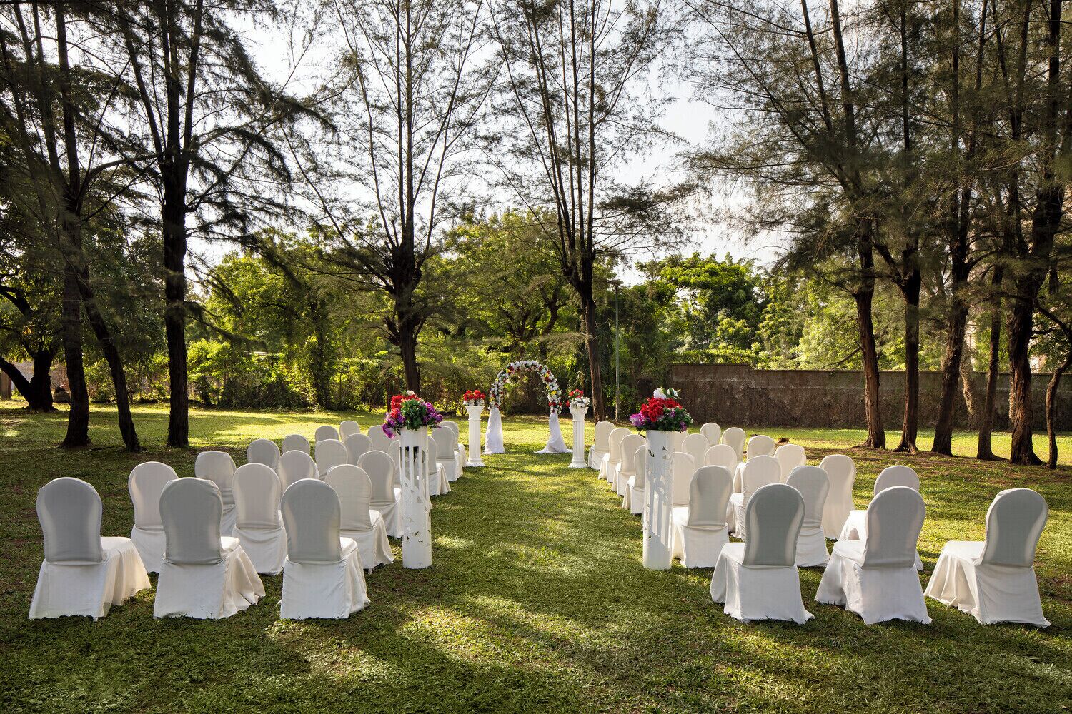 An outdoor wedding venue with rows of white chairs and floral centerpieces.