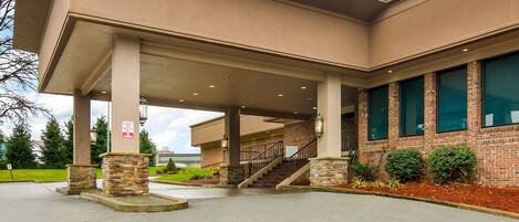 A building with a covered entrance, stone pillars, and a brick facade.