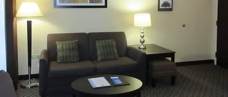 Ein Hotelzimmer mit einer Couch, einem kleinen Tisch, einer Lampe und einem gerahmten Bild an der Wand.