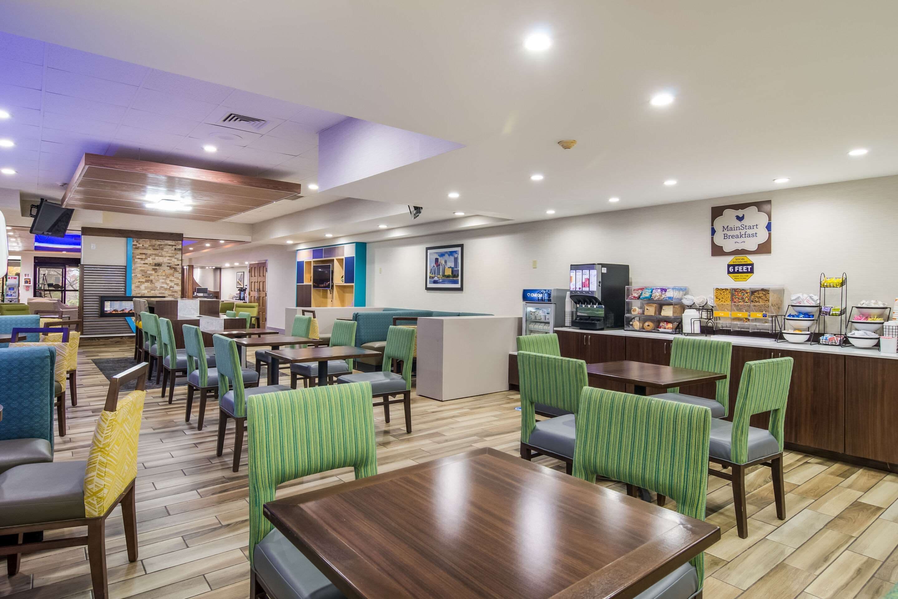A modern hotel lobby with multiple seating areas, a reception desk, and a breakfast bar.