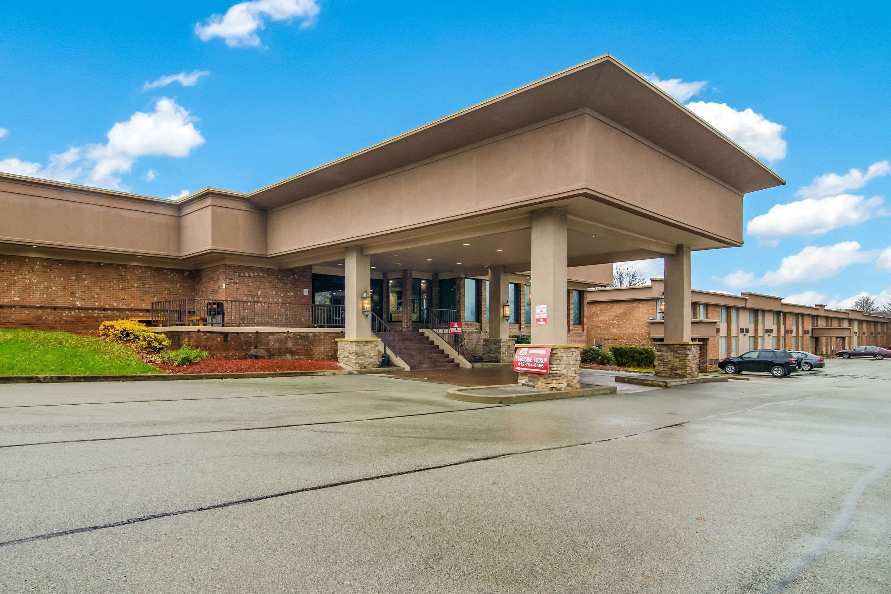 A hotel with a covered entrance, a brick facade, and a parking lot.