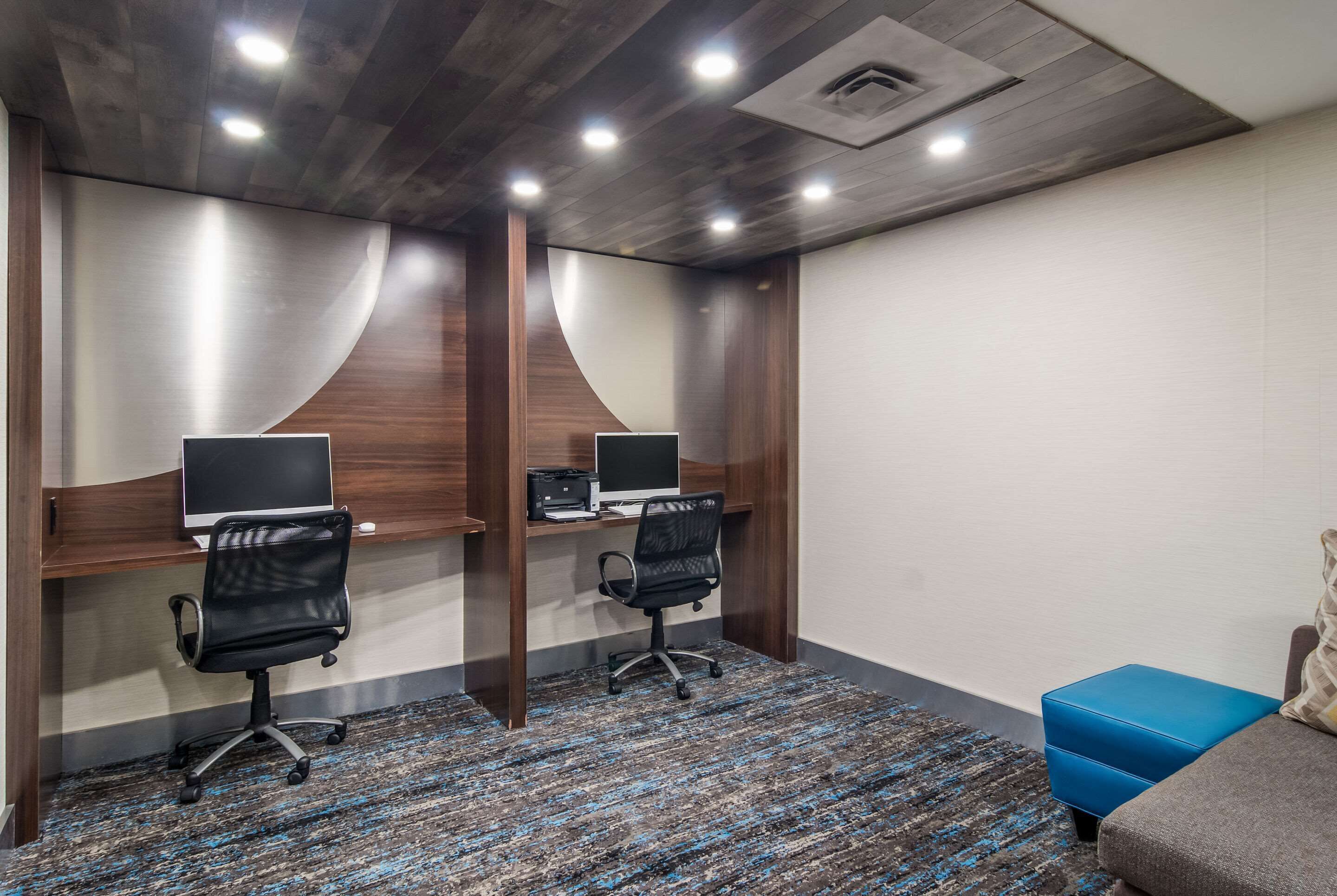 Un salón de conferencias con dos escritorios, cada uno con una computadora y una silla, y un otoman azul.