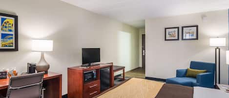 A hotel room with a bed, desk, chair, TV, minibar, and two framed pictures on the wall.