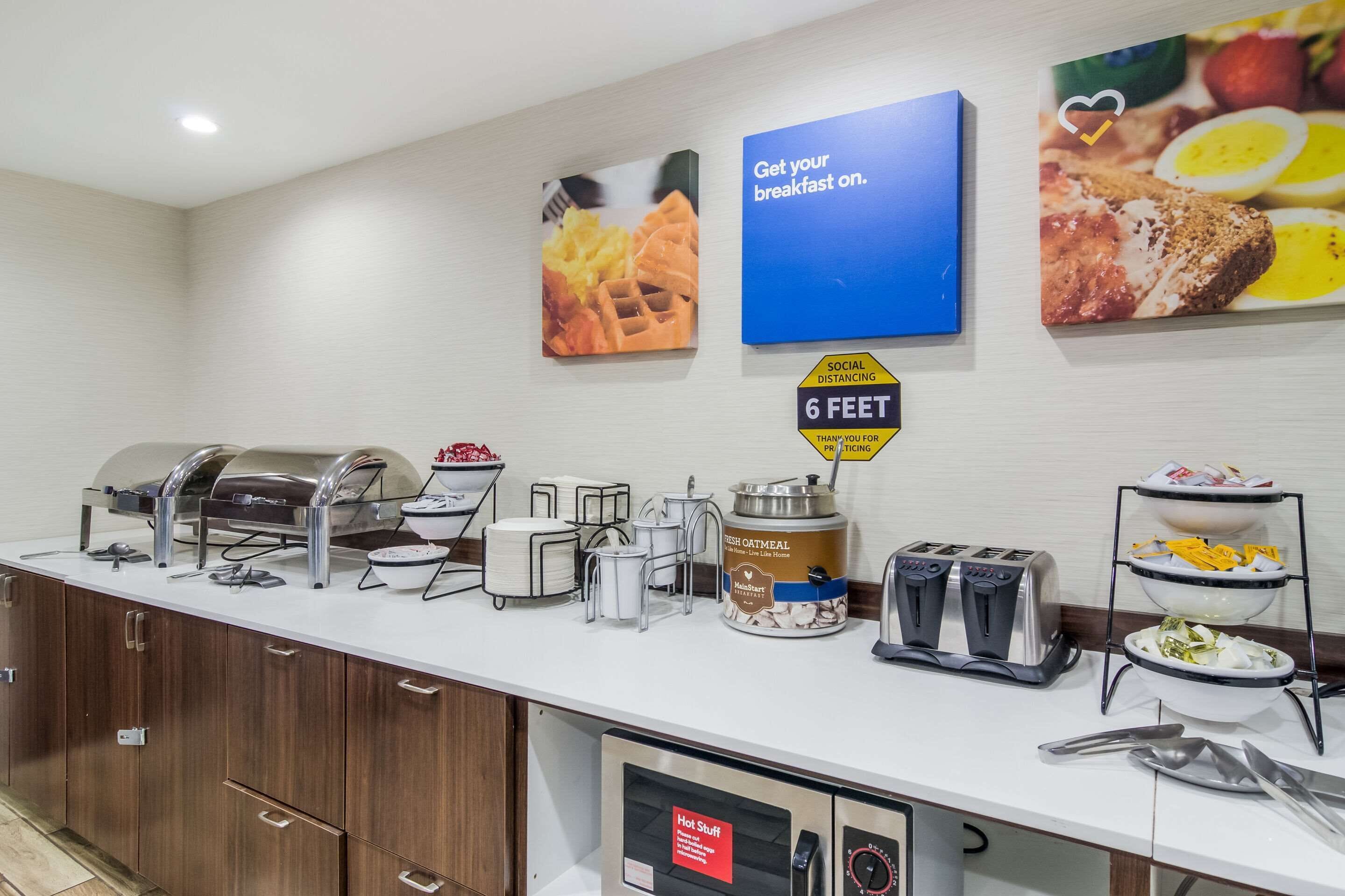 A breakfast buffet with various food items, a sign indicating social distancing, and a sign for hot food.