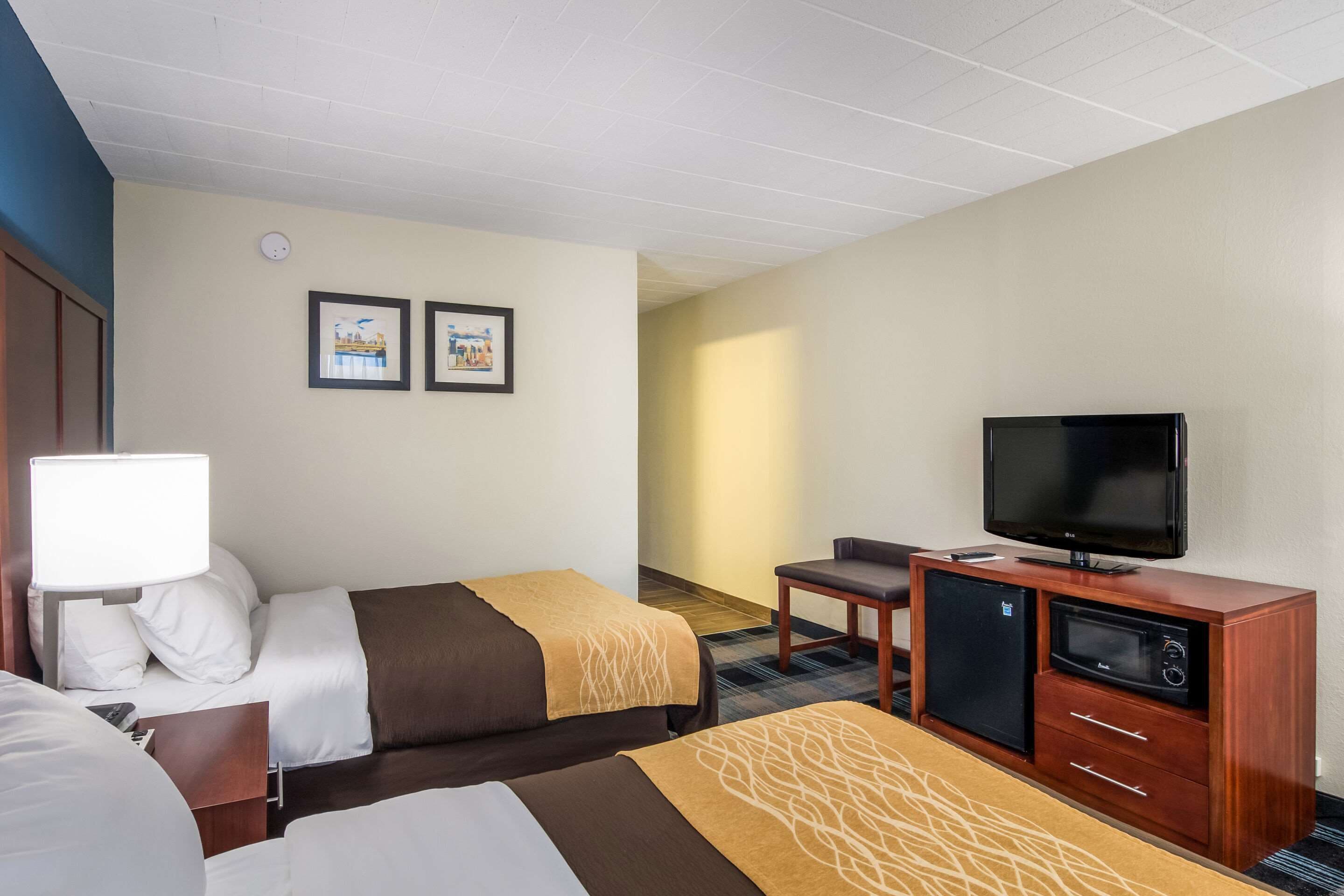 A hotel room with two beds, a TV, a small refrigerator, and a desk with a chair.