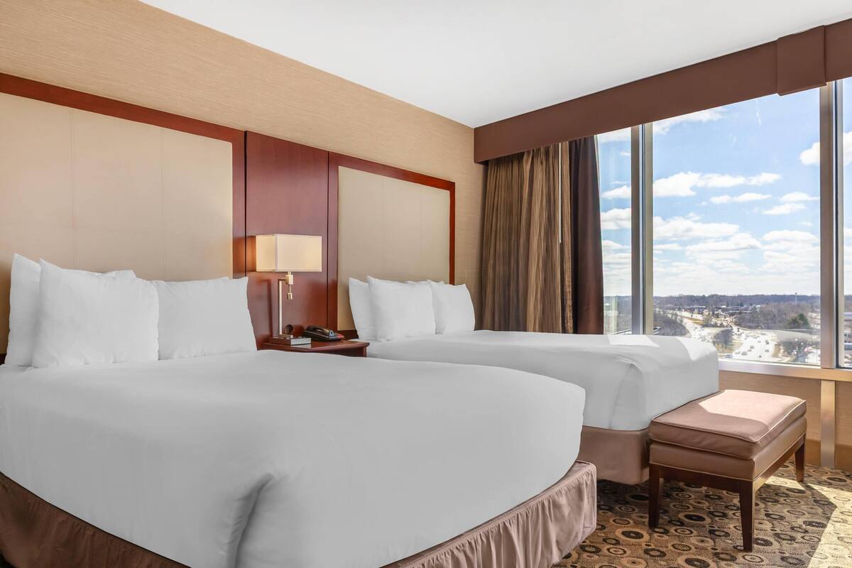 Une chambre d’hôtel avec deux lits, une petite table, une lampe et une grande fenêtre donnant sur la ville.