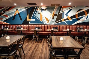 Un restaurante con asientos tipo cabina y mesas, con un mural geométrico en la pared.