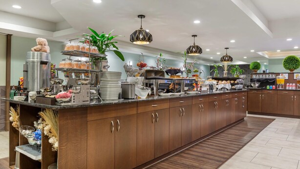 A modern kitchen with a central island, stainless steel appliances, and a variety of food items displayed on shelves.