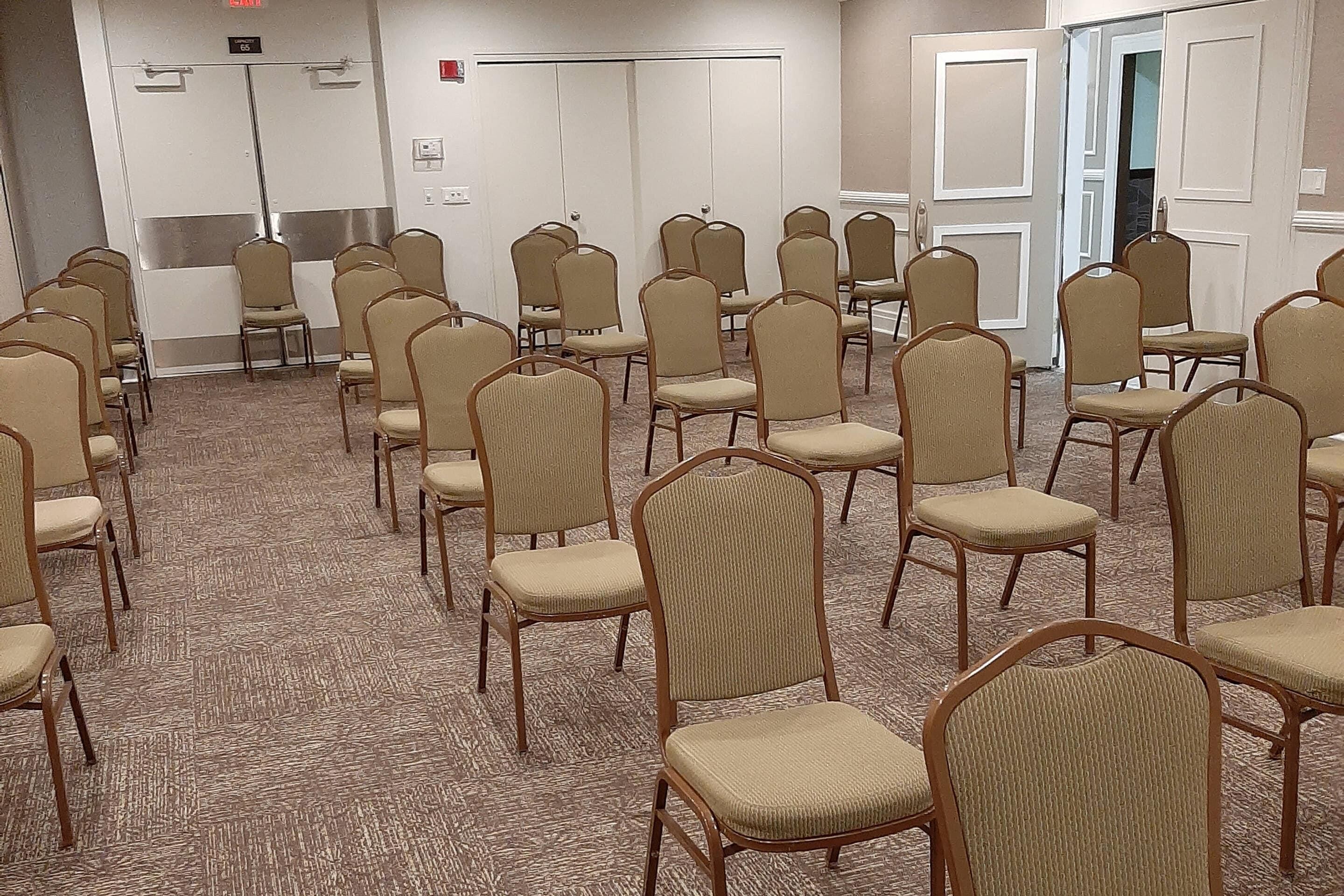 Une salle de conférence avec des rangées de chaises beiges et un sol recouvert de moquette.