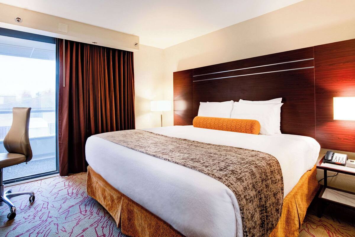 Une chambre d’hôtel avec un grand lit, un bureau avec un téléphone, une chaise, une fenêtre avec des rideaux et une vue sur l’extérieur.