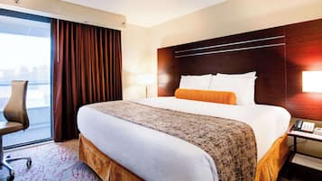 A hotel room with a large bed, a desk with a phone, a chair, a window with curtains, and a view of the outside.
