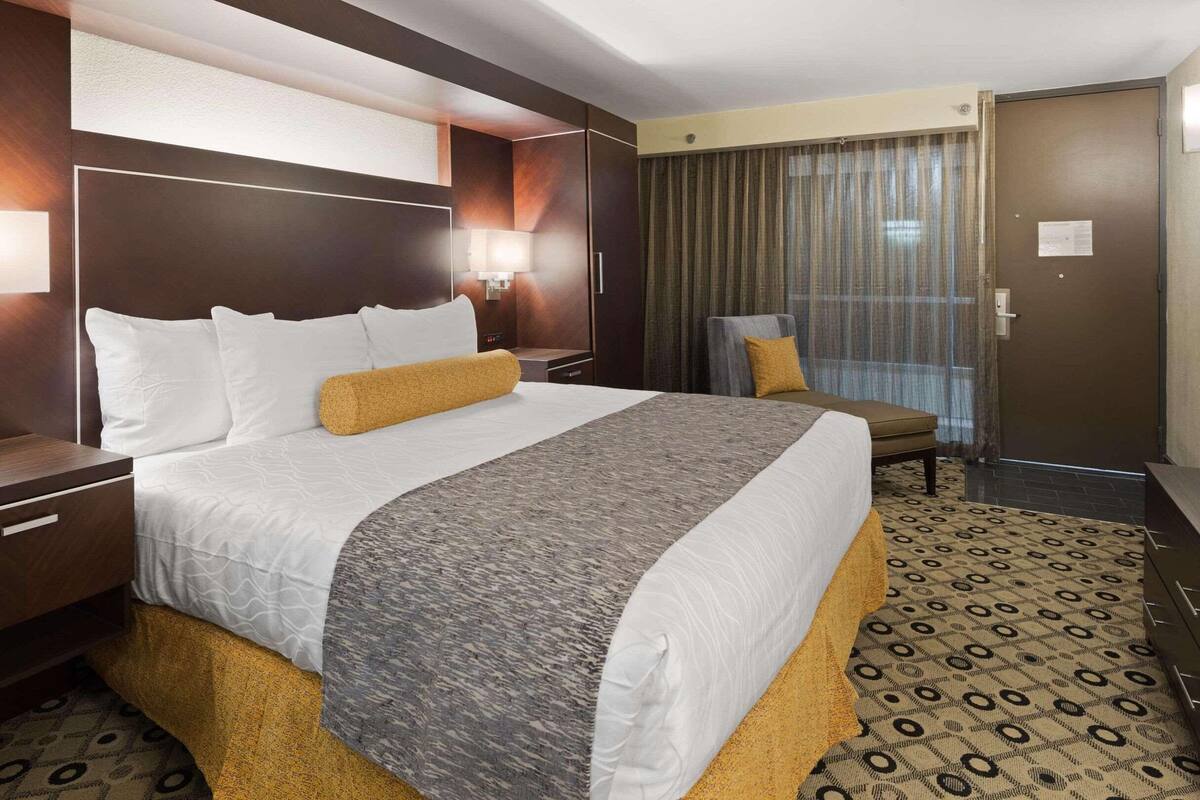 Une chambre d’hôtel avec un grand lit, un bureau, une chaise, une fenêtre avec des rideaux et une porte.