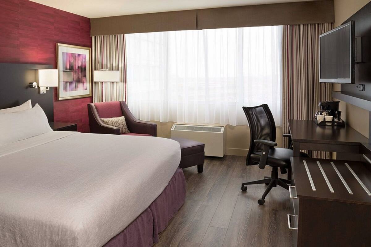 A hotel room with a large bed, a desk with a chair, a TV, and a window with curtains.