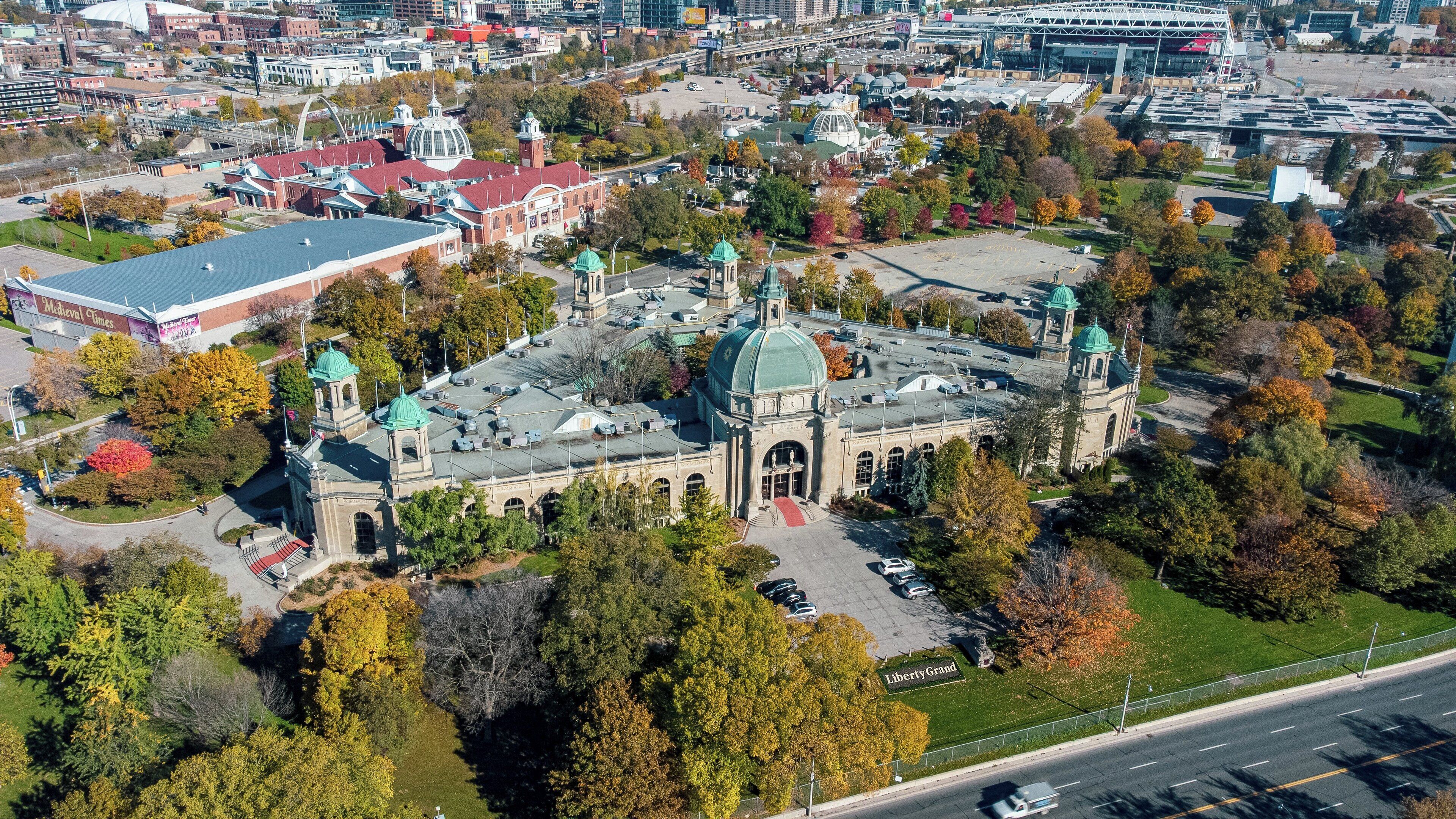 An aerial view of a historic building with a large dome and multiple towers, surrounded by trees and a parking lot.
