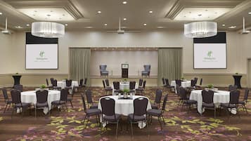 A conference room with multiple tables and chairs, a stage with a podium, and two large screens displaying the Holiday Inn logo.