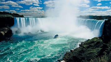 Una cascada imponente con una barca en el agua, rodeada de terreno rocoso y vegetación.
