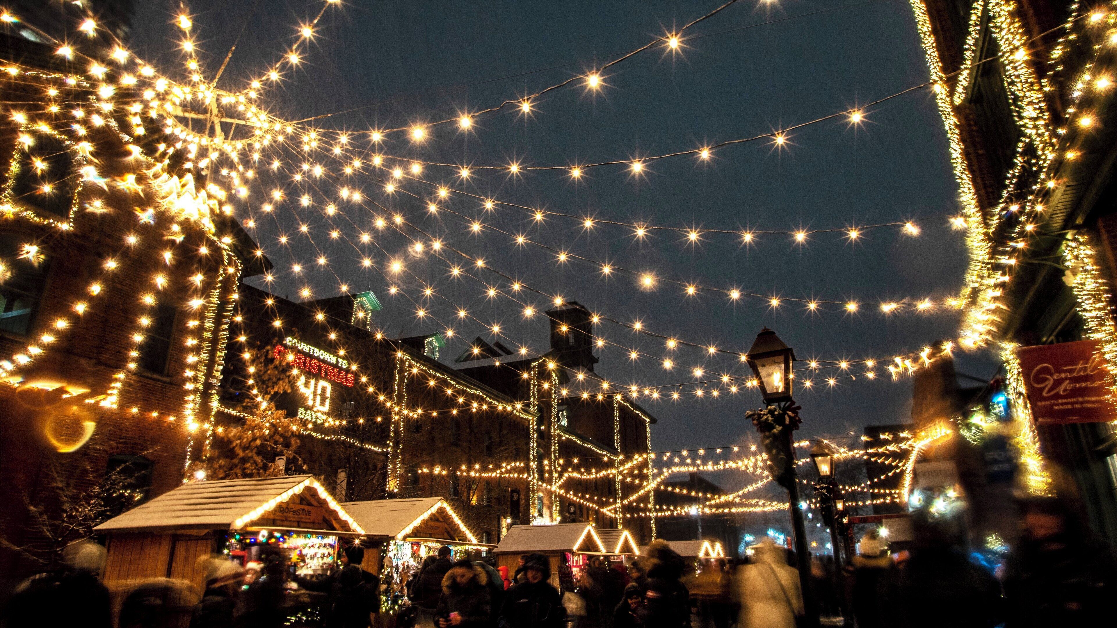 A street decorated with string lights and festive lights, with buildings and a clock tower in the background.
