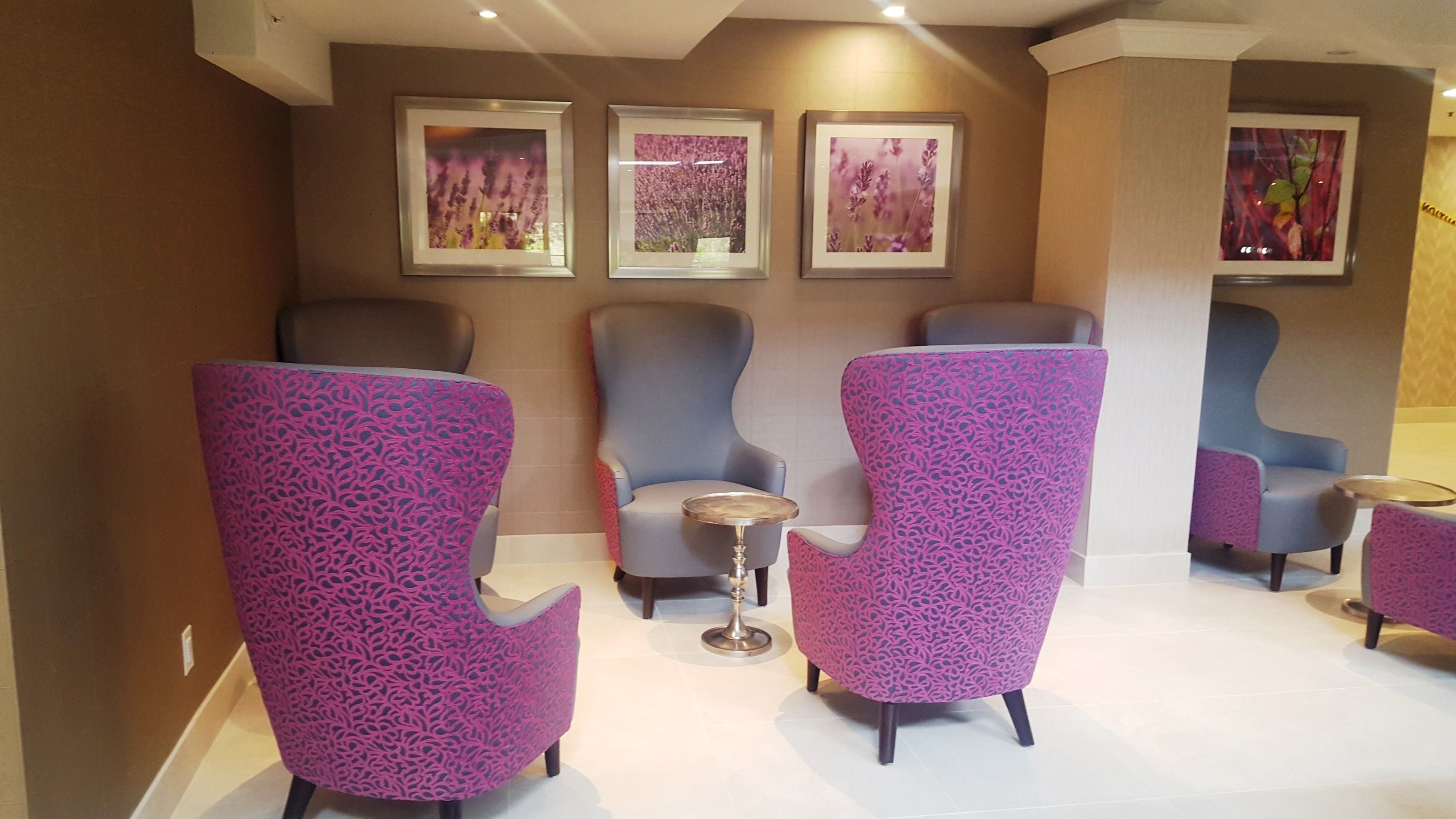 Een zithoek met paarse, gestreepte stoelen en een kleine ronde tafel, een bloemrijk kunstwerk op de muur en een beige muur.