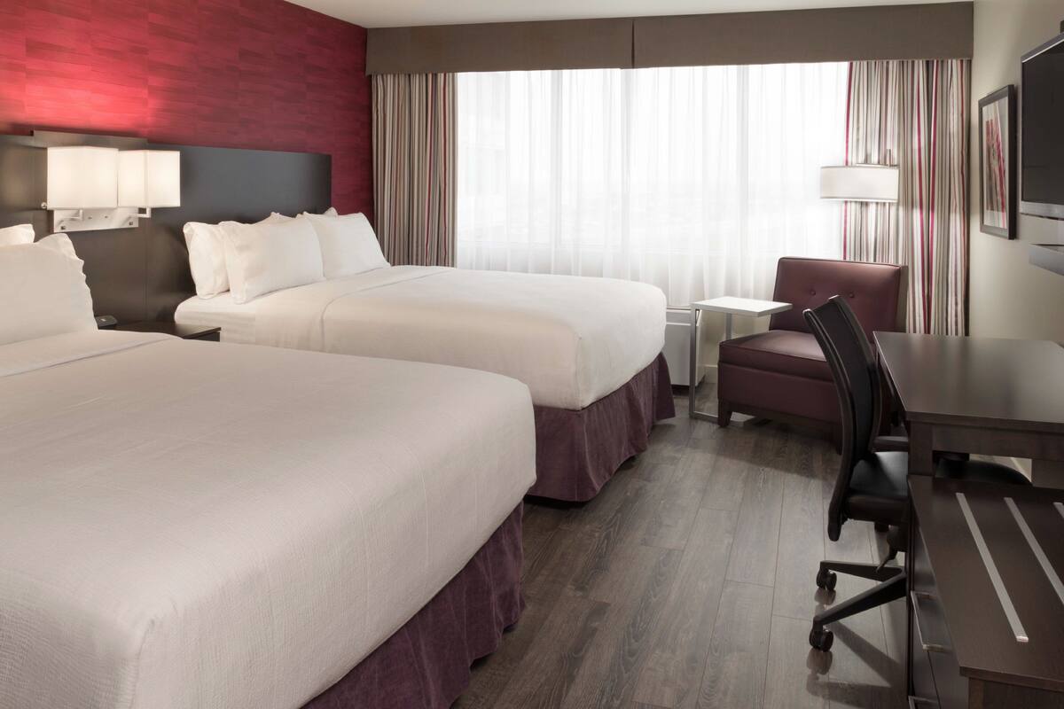 A hotel room with two beds, a desk, a chair, a TV, and a window with curtains.