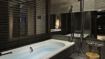 A modern bathroom with a large bathtub, a shower area, and a wooden stool.
