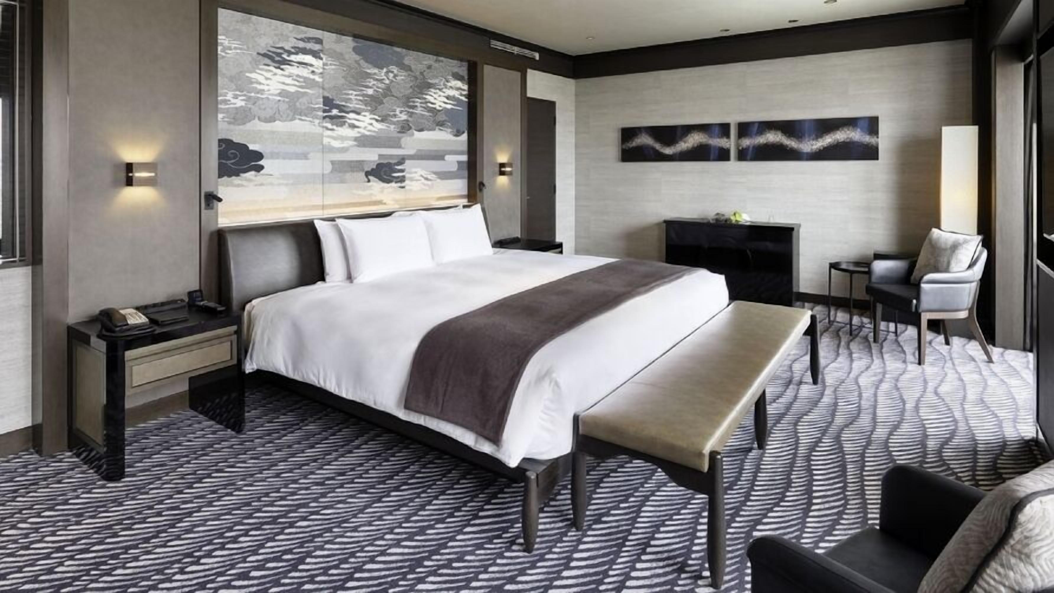 Ett hotellrum med en stor säng, en bänk, ett skrivbord och en öppen spis.
