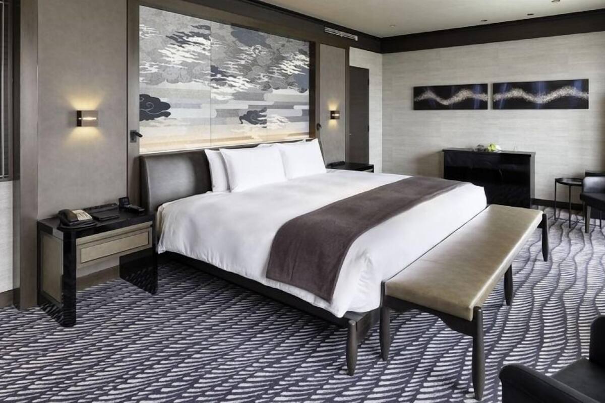 A hotel room with a large bed, a bench, a desk, and a fireplace.