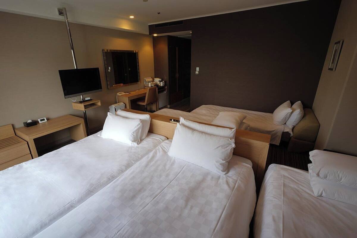 A hotel room with two beds, a desk, a TV, and a mirror.
