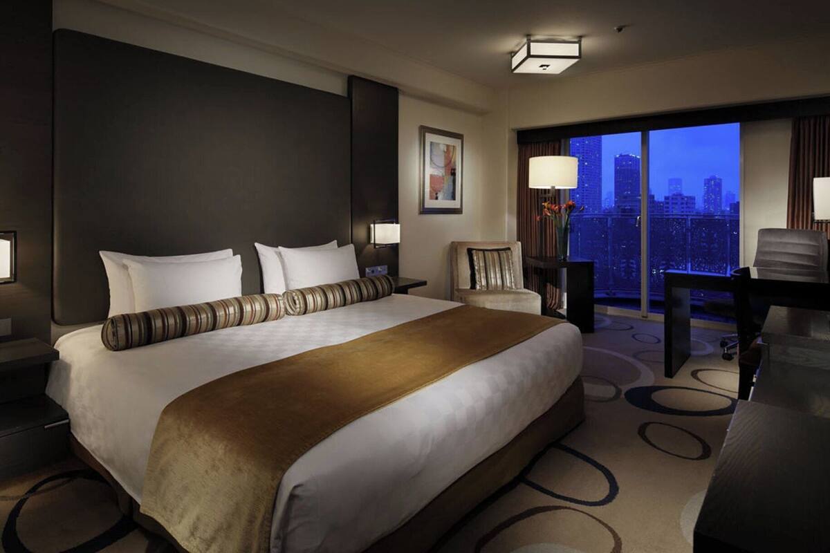 A hotel room with a large bed, a desk, a chair, and a view of the city skyline.