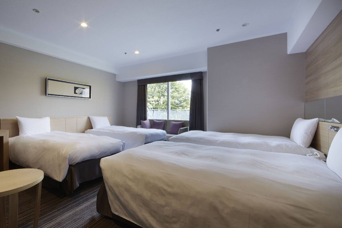 A hotel room with three beds, a small table, and a window with curtains.