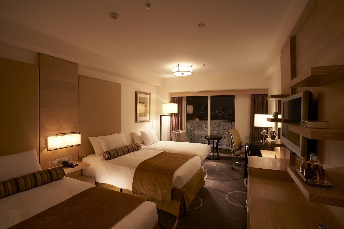 A hotel room with two beds, a desk, a TV, and a balcony with a view.