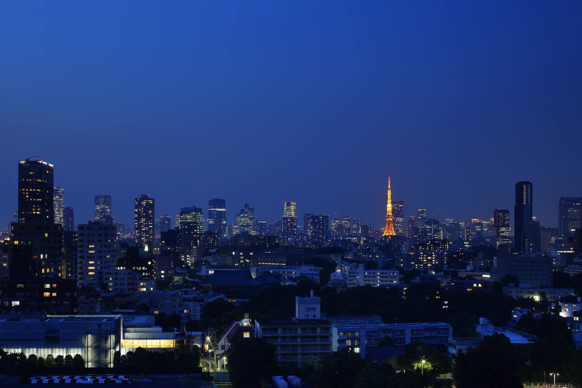 A city skyline at dusk with illuminated buildings and a prominent tower in the center.