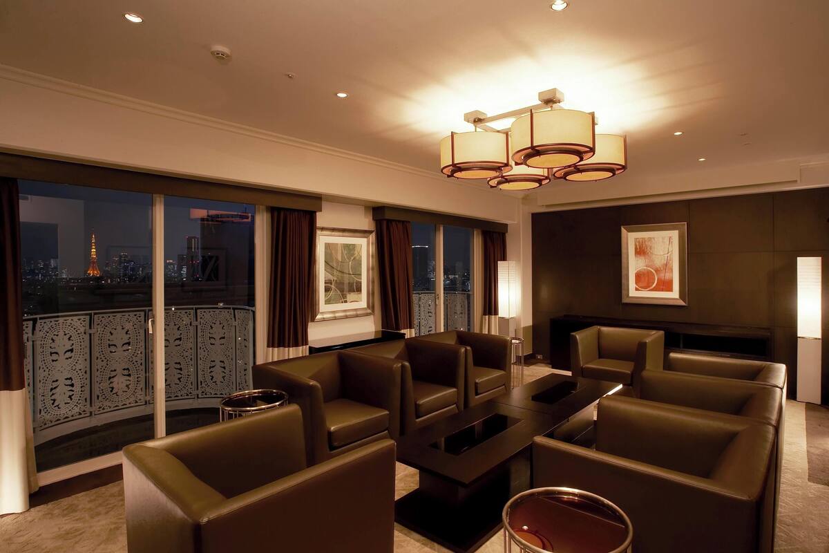 A modern hotel room with a balcony, leather sofas, a flat-screen TV, and a city view.