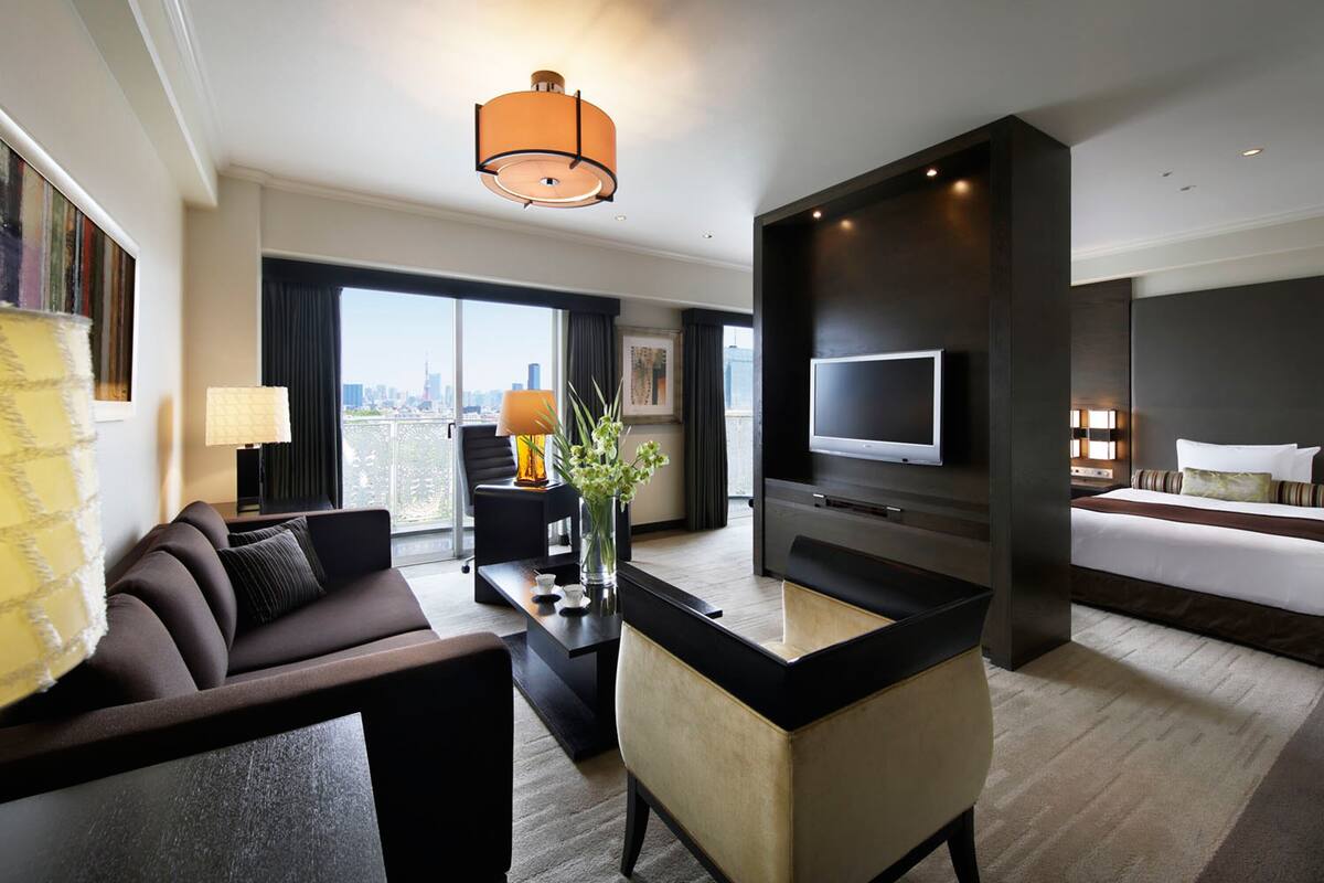 A modern hotel room with a sofa, a coffee table, a TV, and a bed.