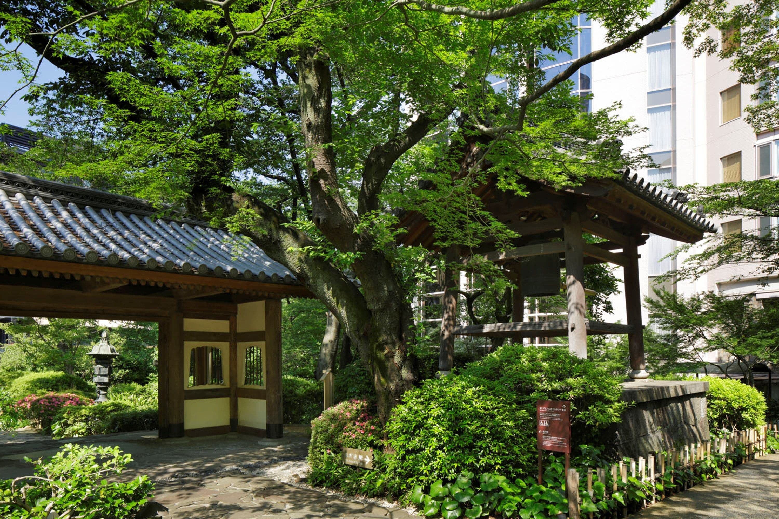 A traditional Japanese garden with a wooden pavilion, stone lantern, and lush greenery.