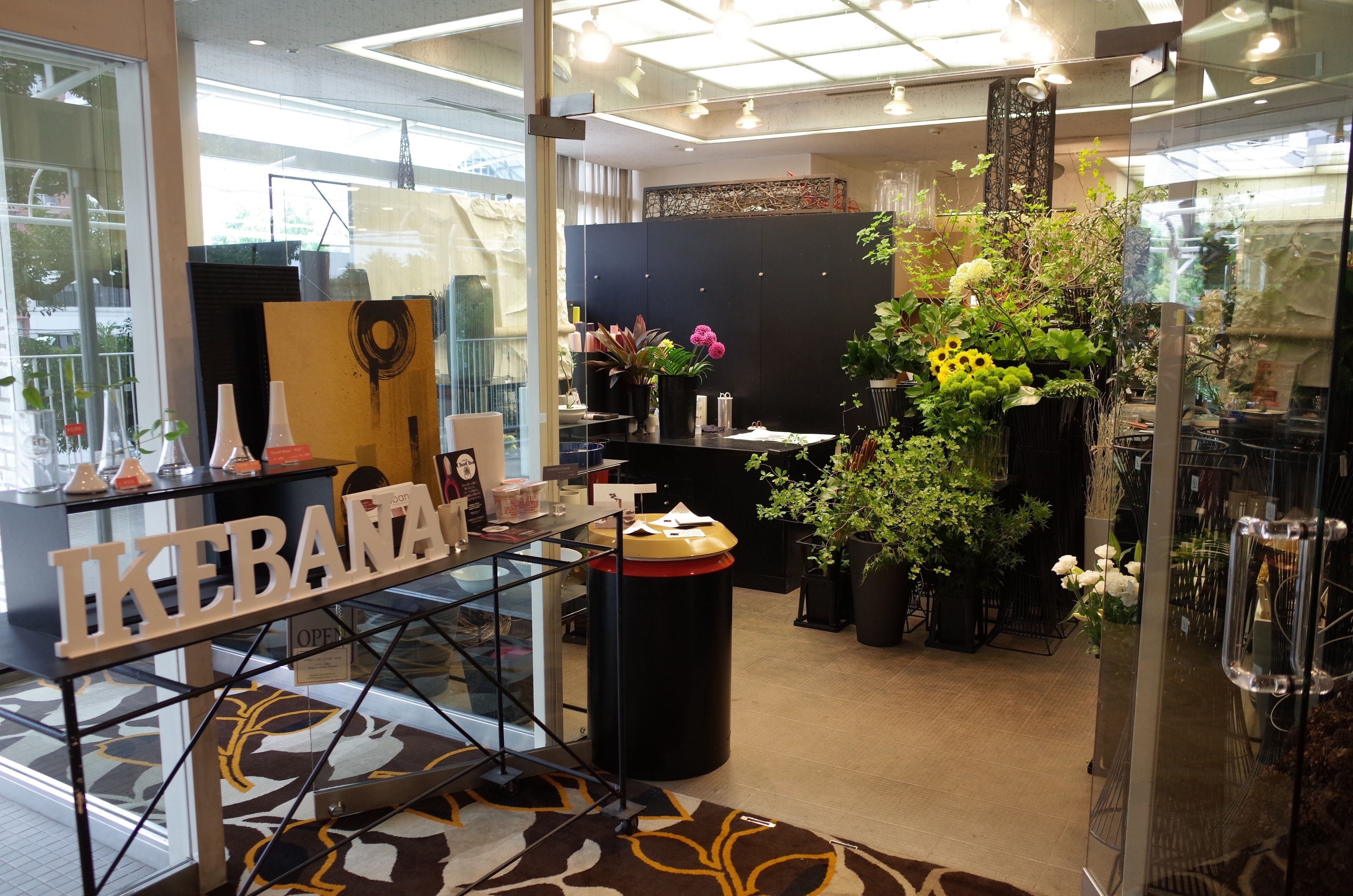 A reception area with a glass partition, a reception desk, and a display of potted plants and flowers.