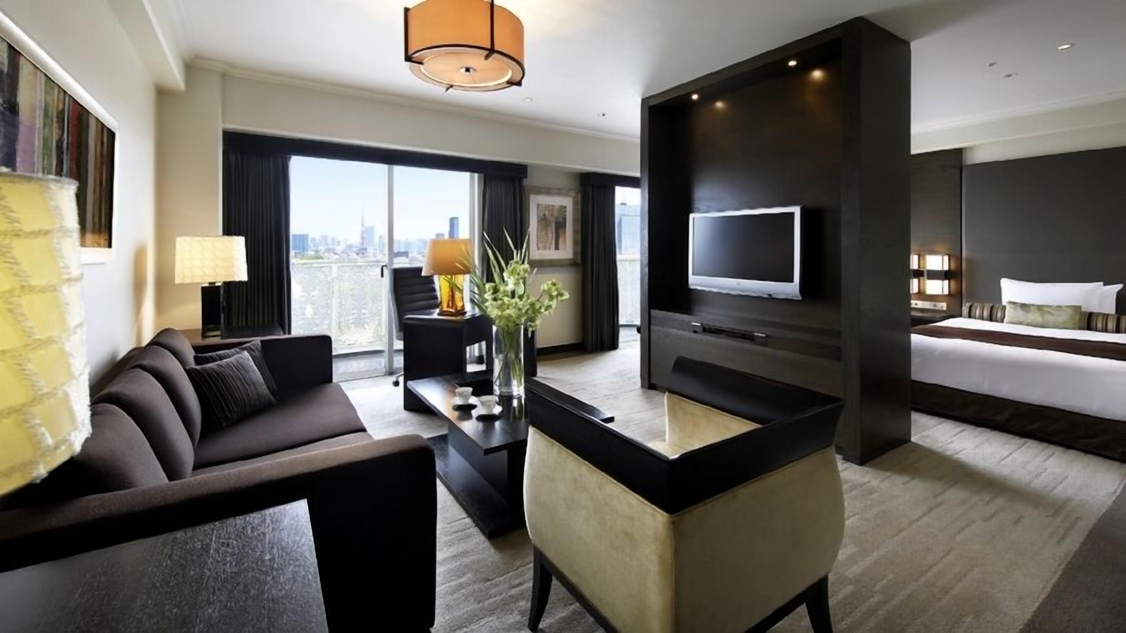 Ett modernt hotellrum med en soffa, ett skrivbord, en TV, en säng och utsikt över staden.