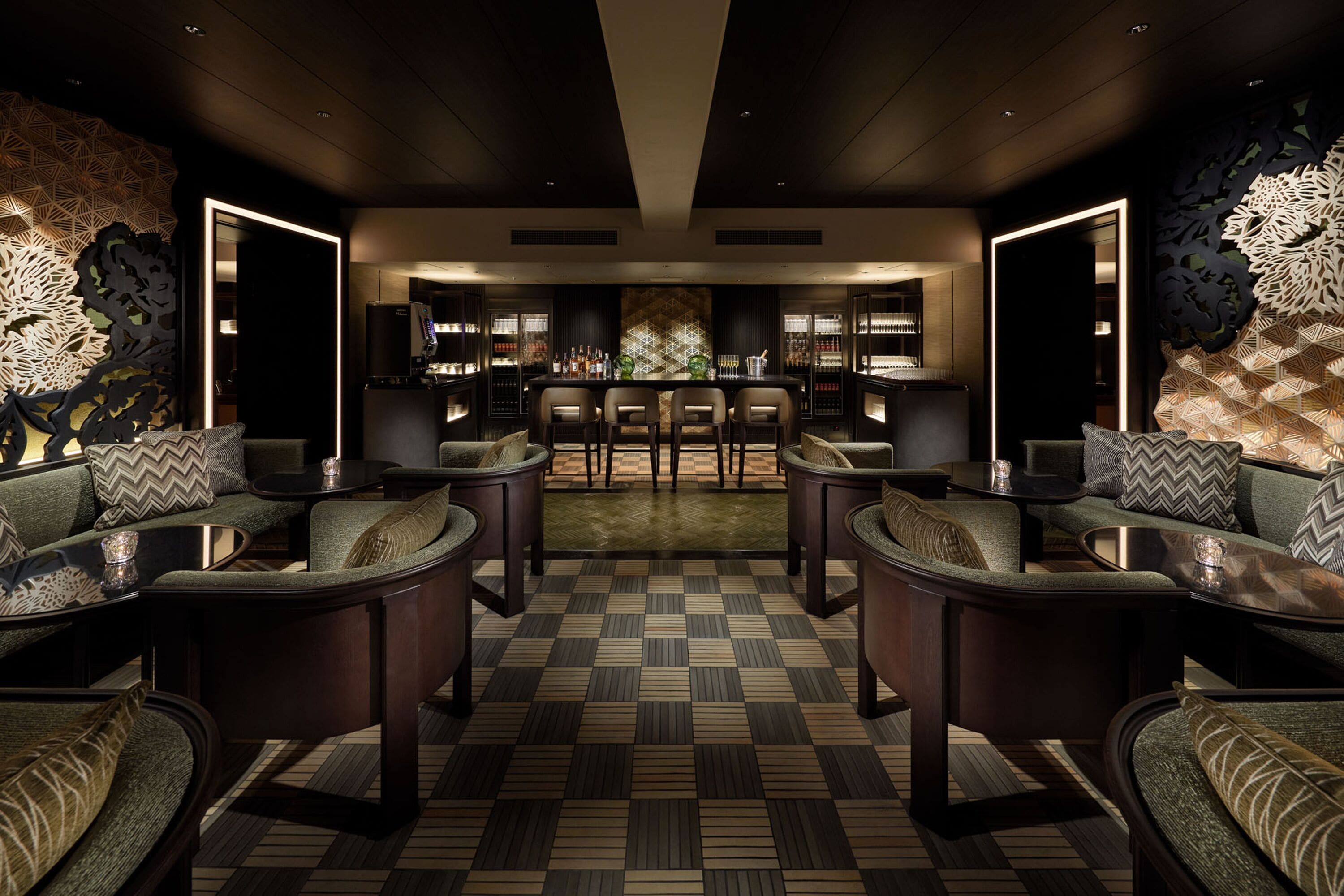 A modern lounge area with a checkered floor, dark wood furniture, and a bar in the background.