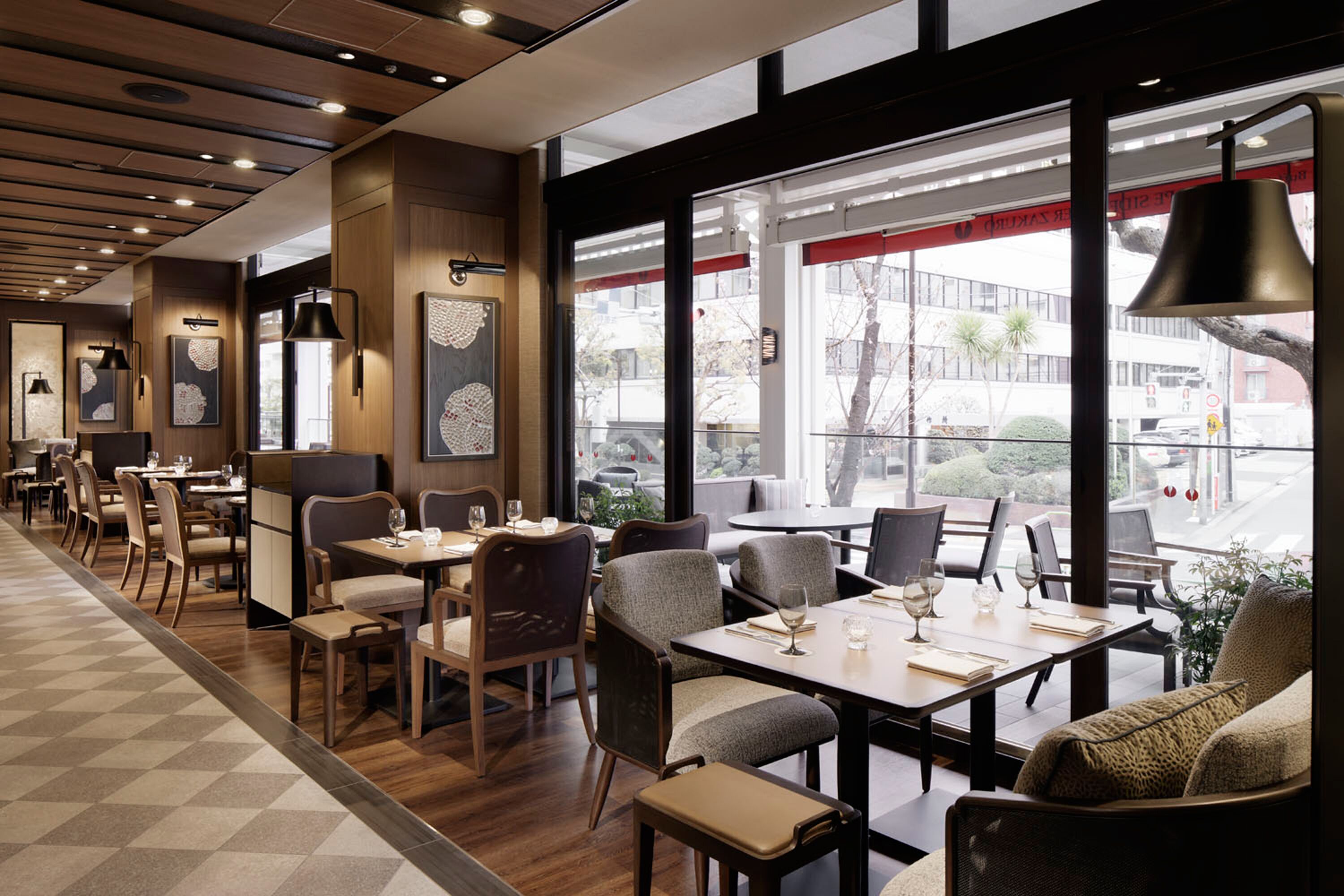 Un restaurante con suelo de madera, mesas con sillas y ventanas amplias que dan a la calle.