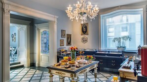 A spacious room with a large dining table set for breakfast, a chandelier, and a view of the city through a large window. - Grand Hotel Santa Lucia (Naples)