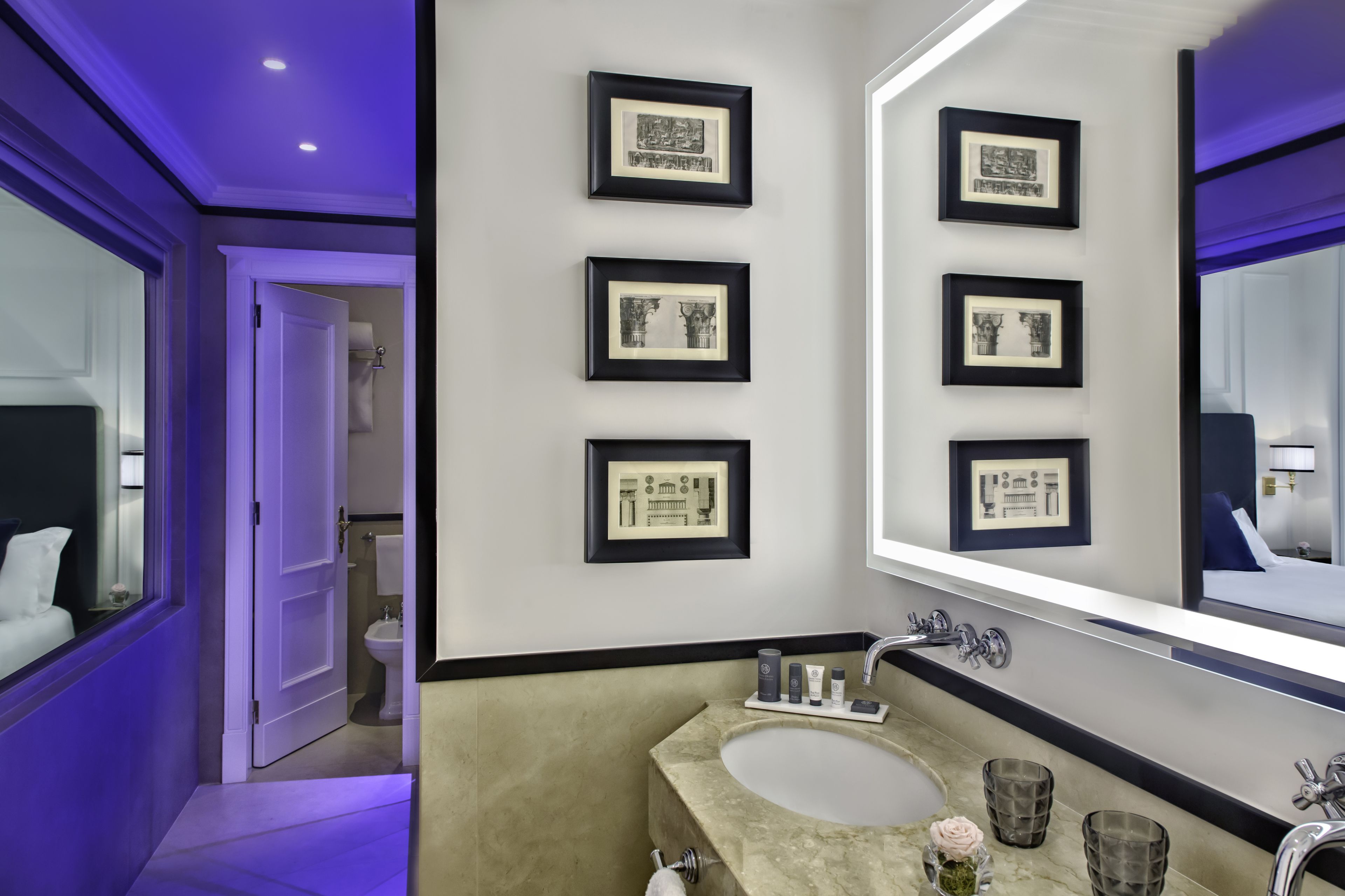 Une salle de bain moderne avec un grand miroir, des œuvres d’art encadrées et un lavabo en marbre.