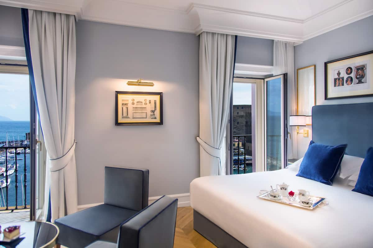 Une chambre d’hôtel dotée d’un grand lit, d’un coin salon et d’un balcon offrant une vue sur la mer.