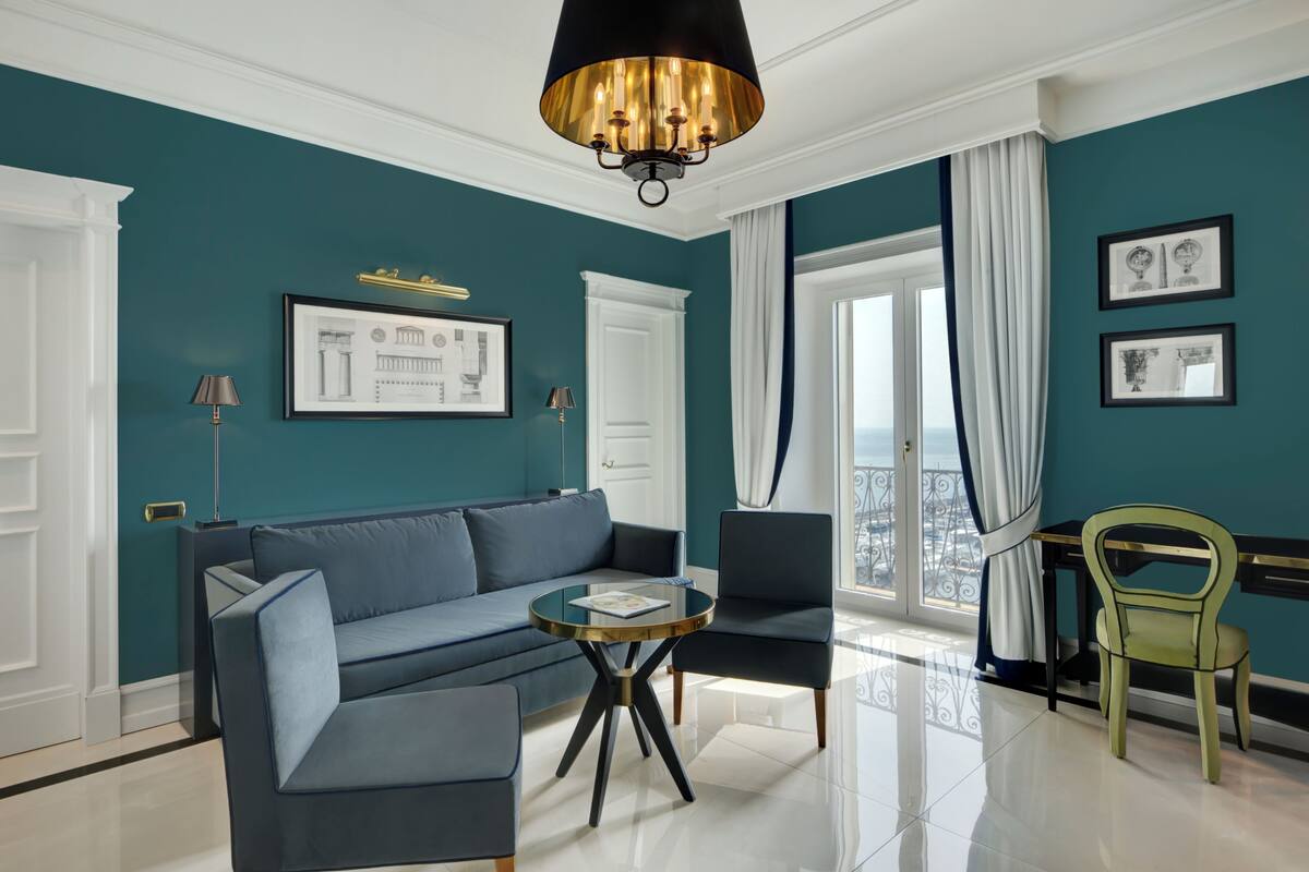 Un salon moderne avec des murs de couleur turquoise, un canapé, des fauteuils, une table basse en verre et un lustre.