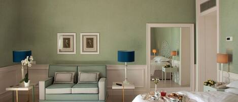 A hotel room with a green wall, a sofa, a bed, a tray with breakfast, and two framed pictures on the wall.